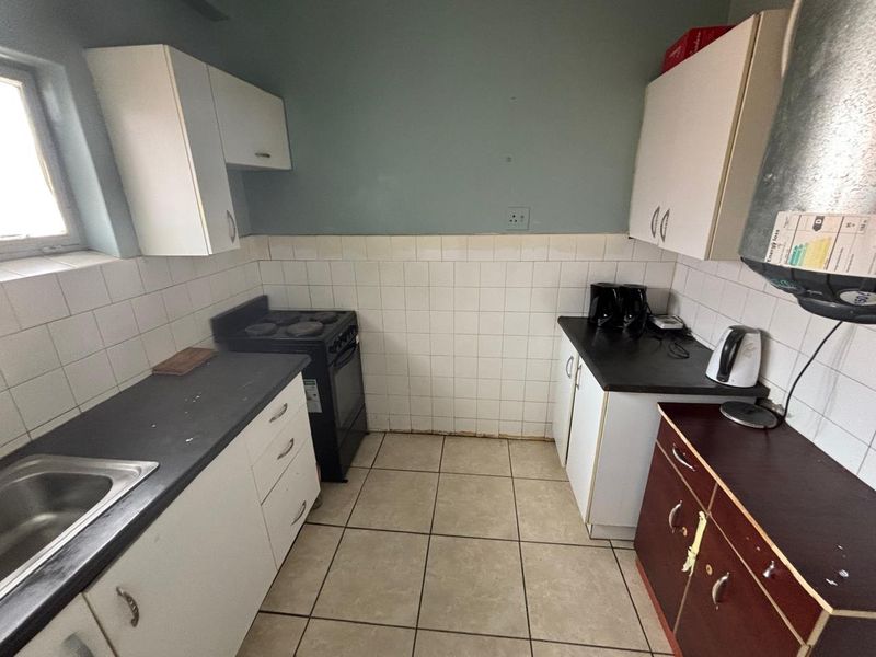 A functional kitchen featuring built-in cabinetry, laminate countertops, a stainless steel sink, and a freestanding stove, with tiled walls and flooring throughout.