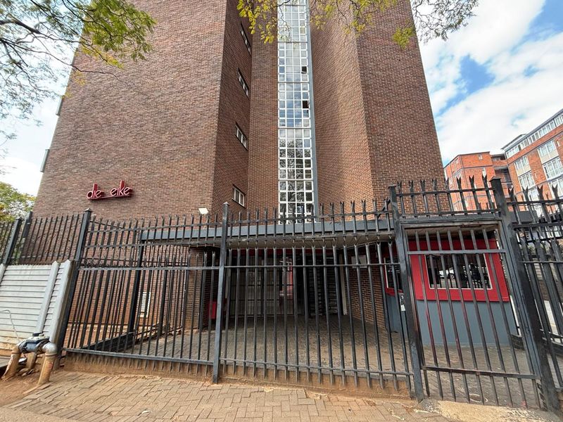 Front exterior view of the apartment building featuring a brick facade, secure metal fencing, and a dedicated security guard booth at the entrance.