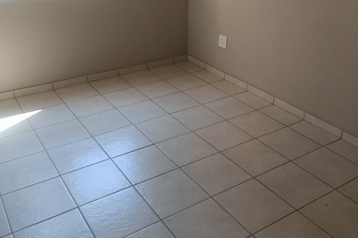 A clean, empty bedroom featuring neutral tiled flooring and a large window, providing a bright and versatile space ready for personalization.