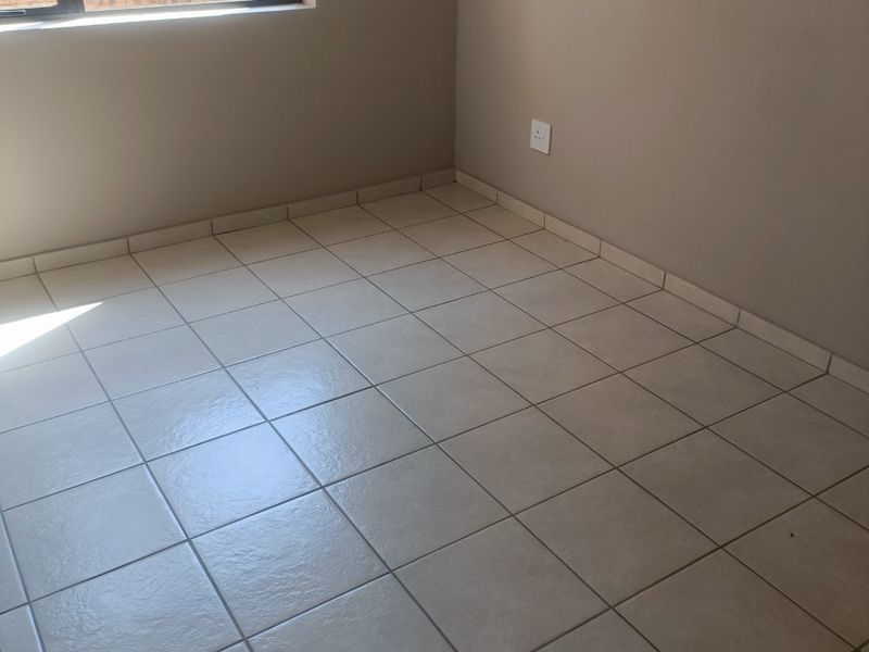 A clean, empty bedroom featuring neutral tiled flooring and a large window, providing a bright and versatile space ready for personalization.