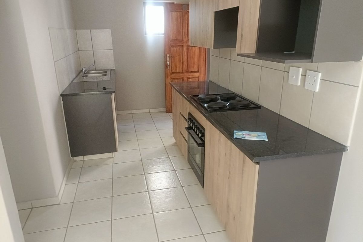 A clean, functional kitchen featuring modern wood-tone cabinetry, granite countertops, a built-in oven and hob, and neutral tiled flooring.