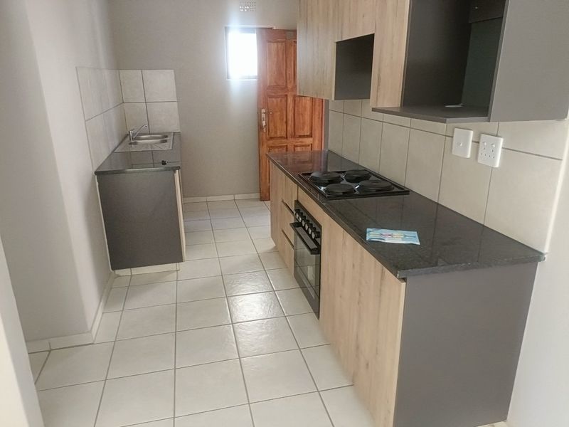 A clean, functional kitchen featuring modern wood-tone cabinetry, granite countertops, a built-in oven and hob, and neutral tiled flooring.