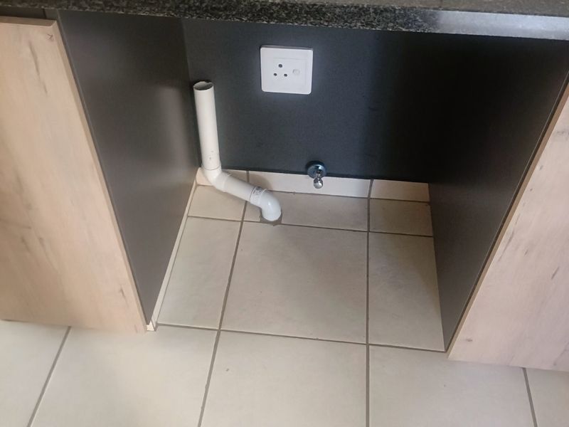 A kitchen under-counter space featuring a granite countertop, stainless steel sink, and dedicated plumbing and electrical connections for an appliance.