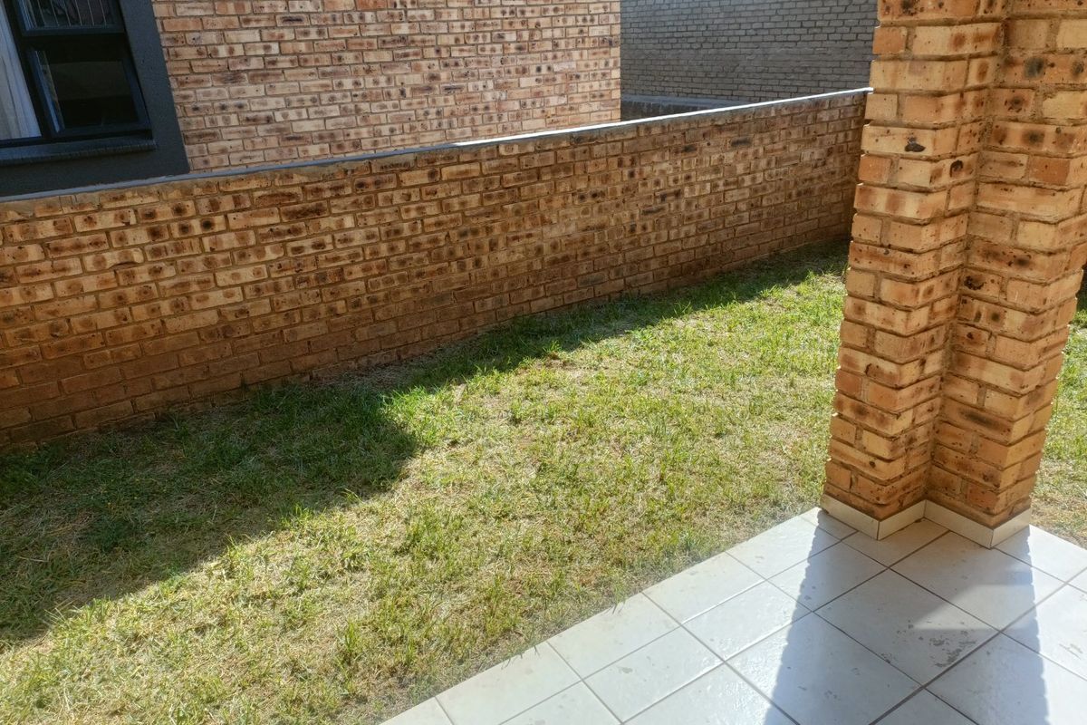 A private rear courtyard featuring a tiled patio area, face brick boundary walls, and a small grass lawn.