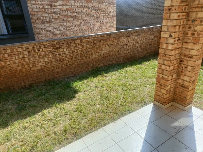A private rear courtyard featuring a tiled patio area, face brick boundary walls, and a small grass lawn.