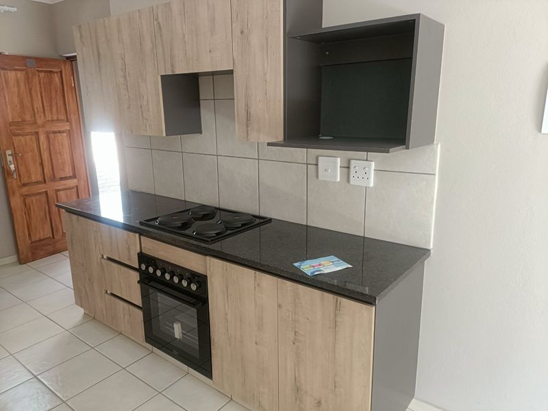 Modern kitchen featuring light wood-grain cabinetry, dark granite countertops, a built-in oven and hob, and neutral tiled flooring.