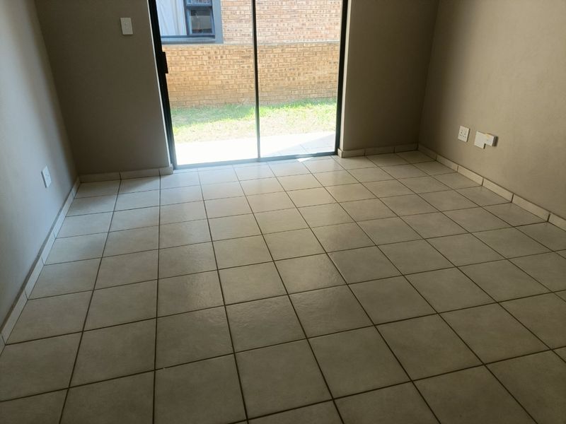 An empty living area featuring neutral ceramic floor tiles and a sliding glass door providing access to the exterior.