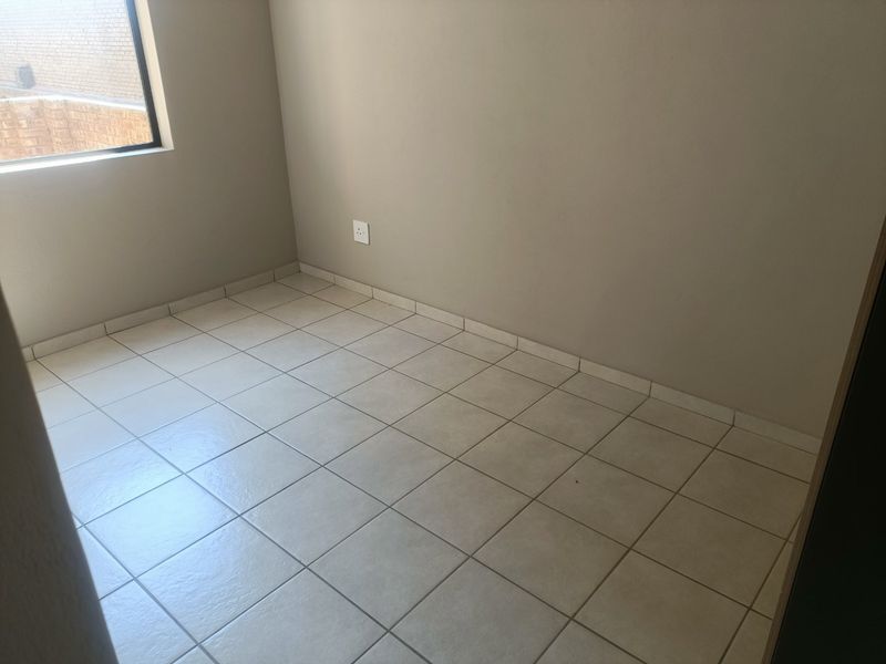 A clean, empty bedroom featuring neutral wall paint and light-colored ceramic floor tiles, providing a blank canvas for personalization.