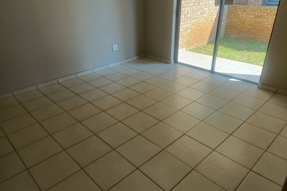 An empty living area featuring neutral tiled flooring and a sliding glass door providing direct access to the outdoor patio and garden area.