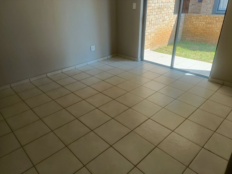 An empty living area featuring neutral tiled flooring and a sliding glass door providing direct access to the outdoor patio and garden area.