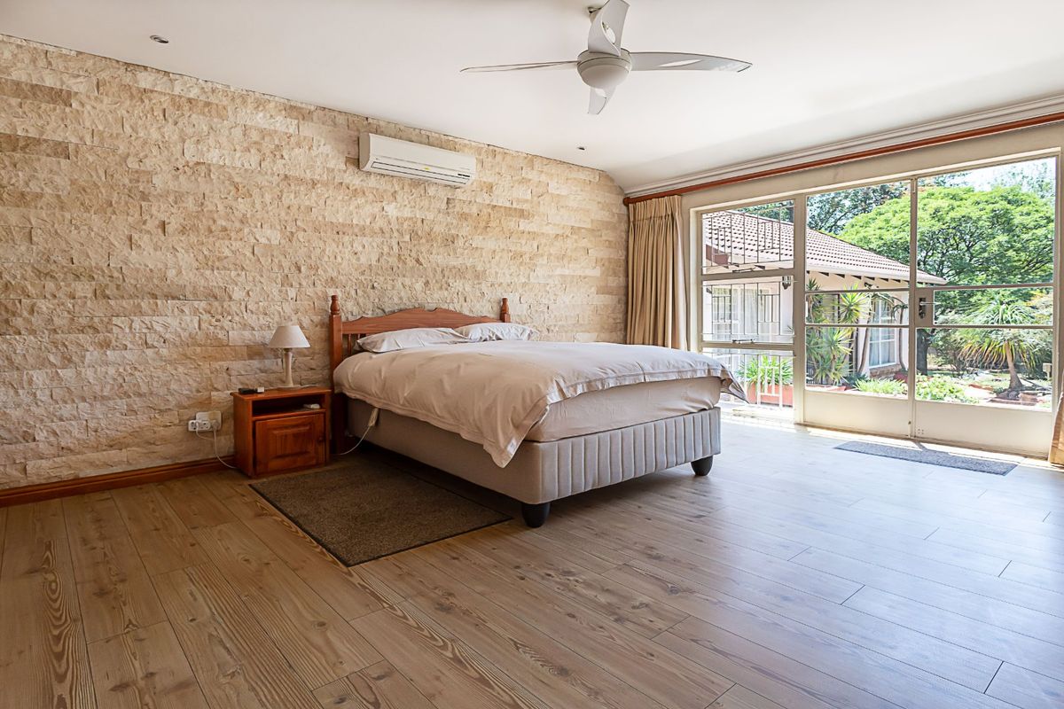 Spacious bedroom featuring a textured stone accent wall, wood-look tile flooring, ceiling fan, air conditioning, and large sliding glass doors opening to the garden.