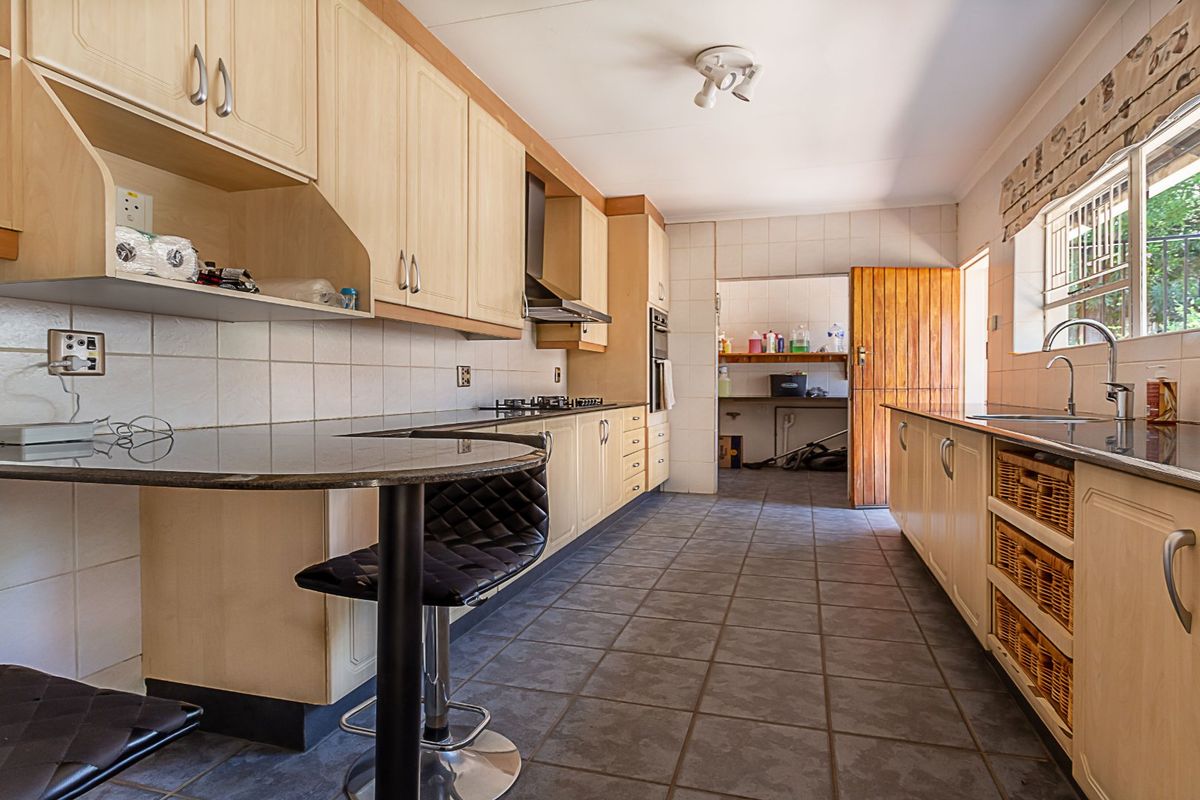 Functional kitchen featuring light wood cabinetry, granite countertops, gas hob, built-in oven, and a convenient breakfast nook, with an adjacent scullery area.