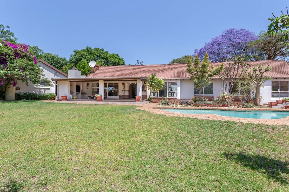Rear view of the property featuring a spacious lawn, swimming pool, and a covered patio area with a built-in braai.