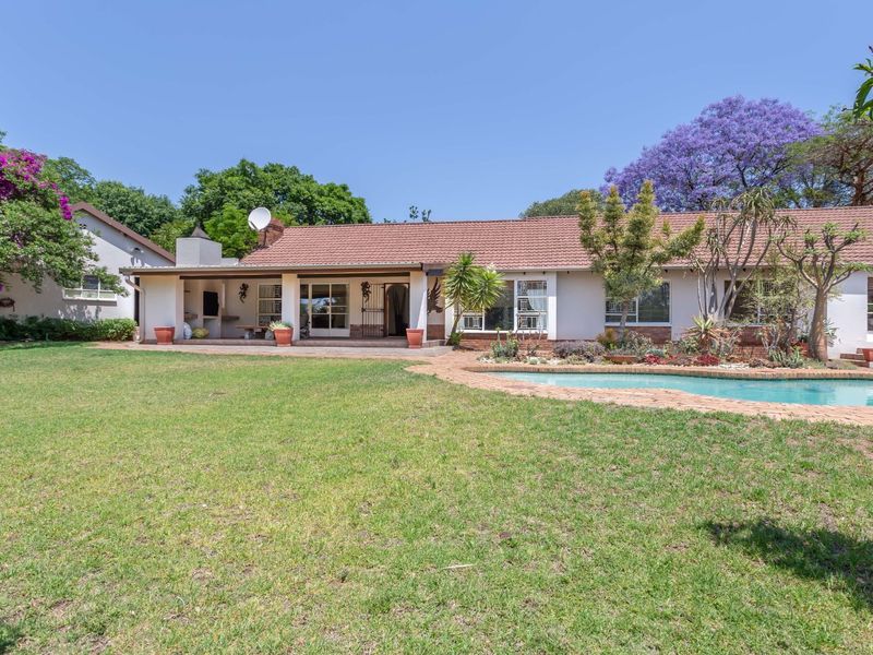 Rear view of the property featuring a spacious lawn, swimming pool, and a covered patio area with a built-in braai.