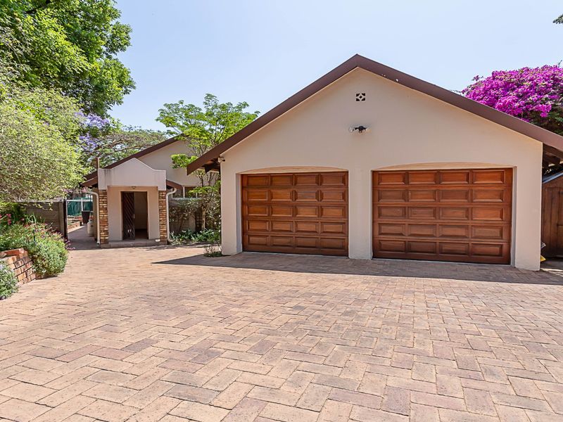 A well-maintained double garage with wooden sectional doors, featuring a spacious paved driveway and established garden surroundings.