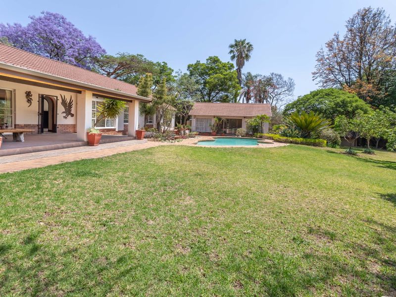 Spacious rear garden featuring a covered patio, a swimming pool with paved surround, and established landscaping.