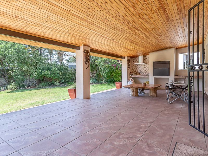 Spacious covered patio featuring a built-in braai, timber-clad ceiling, and tiled flooring, offering a seamless transition to the garden area.