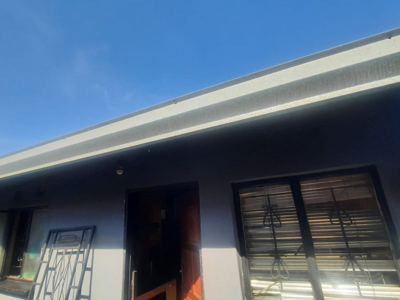 Exterior view of the rear building facade featuring corrugated metal roofing, guttering, and windows with security bars.
