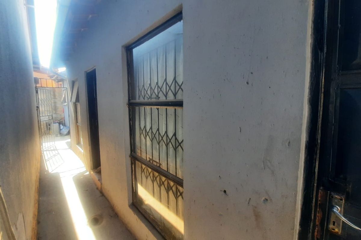 A narrow exterior side passage featuring concrete flooring, security gates, and window security bars along the building facade.