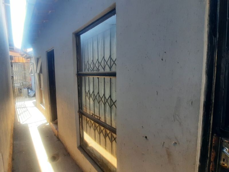 A narrow exterior side passage featuring concrete flooring, security gates, and window security bars along the building facade.