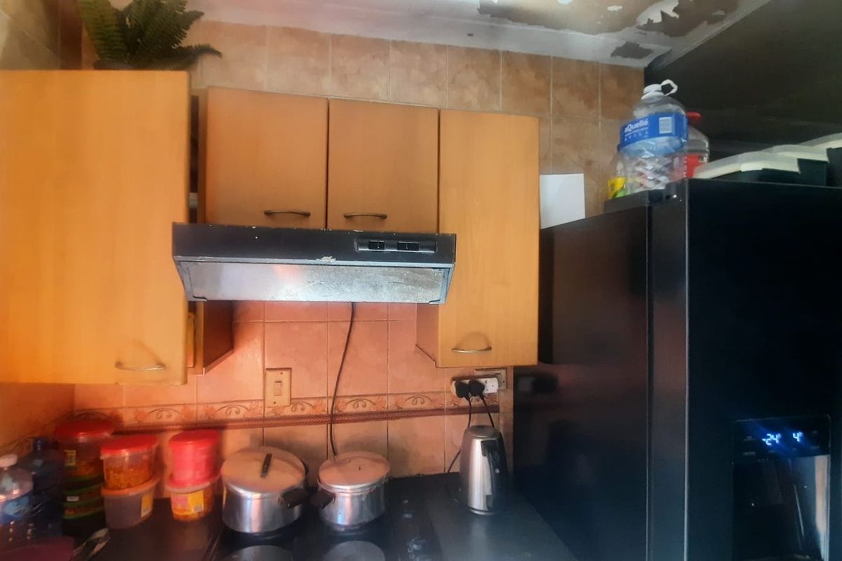 A dated kitchen area featuring wooden cabinetry, a tiled backsplash, and an extractor fan, currently showing signs of ceiling deterioration.