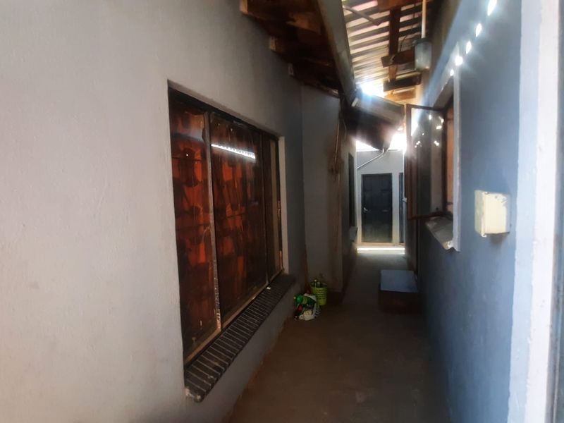 A narrow exterior-facing hallway or walkway featuring exposed timber rafters, tiled window sills, and access to an external door.