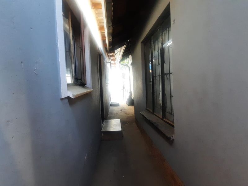 A narrow exterior side passage or walkway between two sections of the building, featuring concrete flooring and security-barred windows.