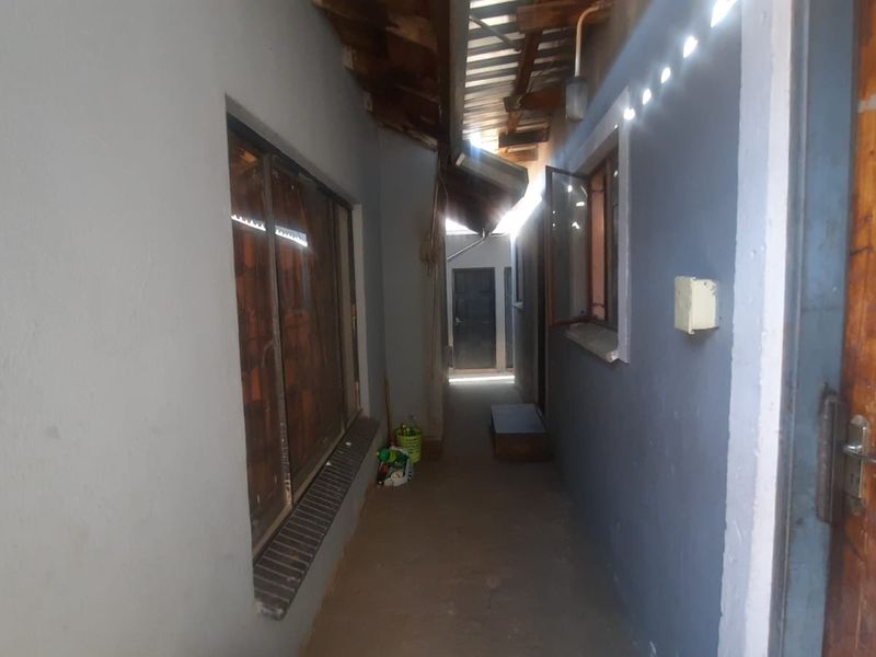 A narrow exterior-facing hallway or walkway featuring exposed timber rafters, metal roofing, and access to multiple entry points.