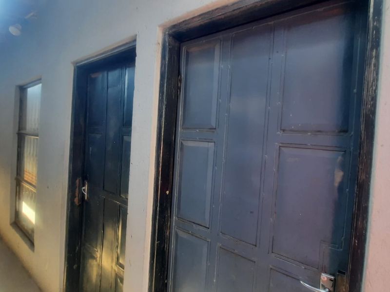 A narrow hallway featuring multiple panelled doors and window frames, showing signs of wear and requiring maintenance.