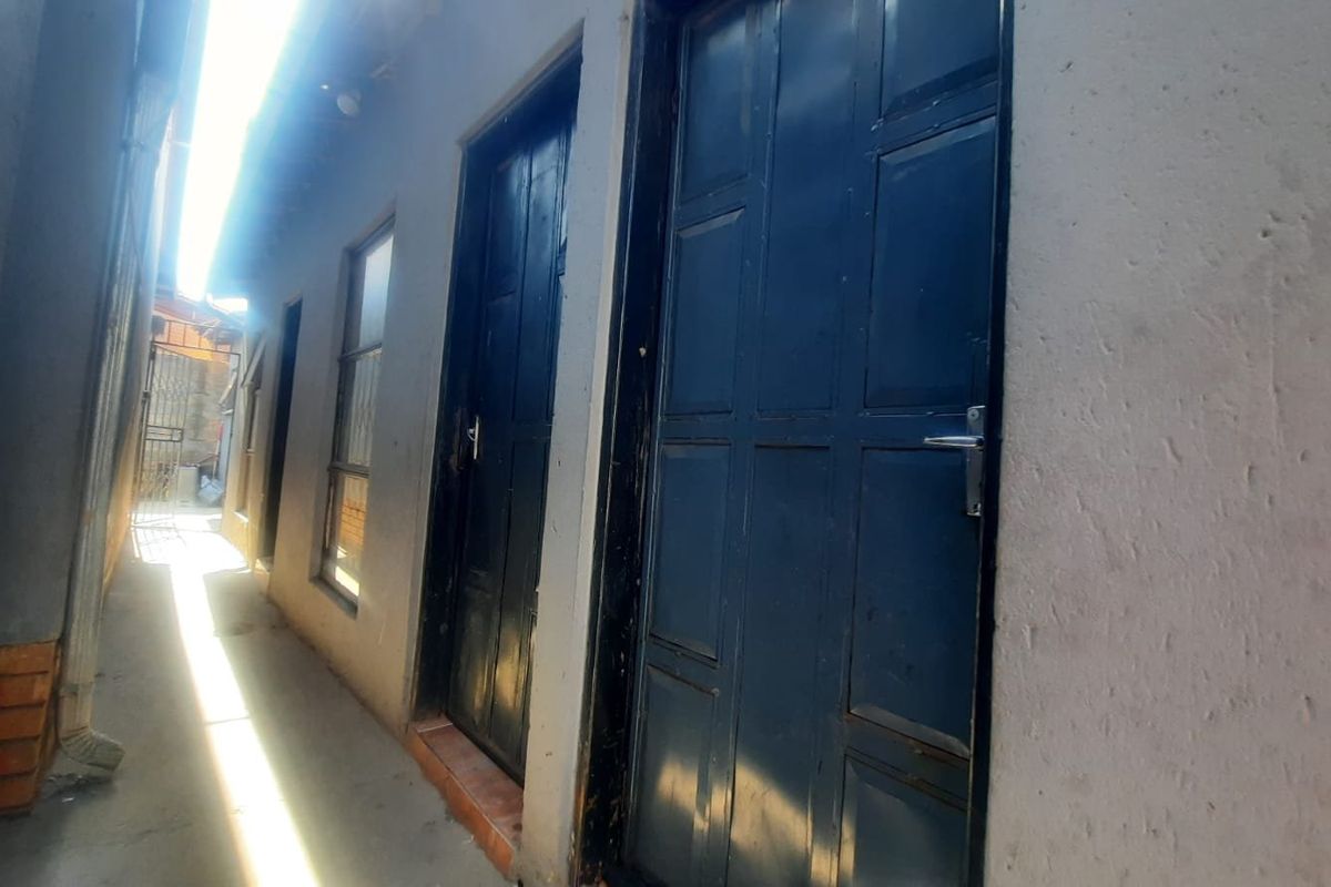 A narrow exterior side passage featuring multiple dark panelled doors and windows along a rendered wall.