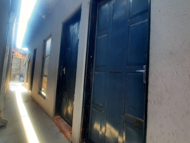 A narrow exterior side passage featuring multiple dark panelled doors and windows along a rendered wall.