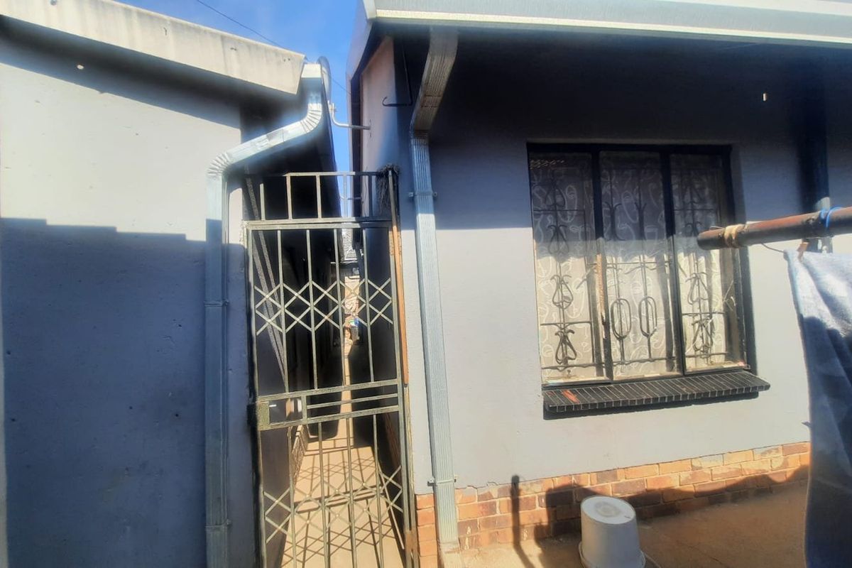 Rear exterior view of the property featuring a security gate, metal security bars on the window, and brick plinth detailing.