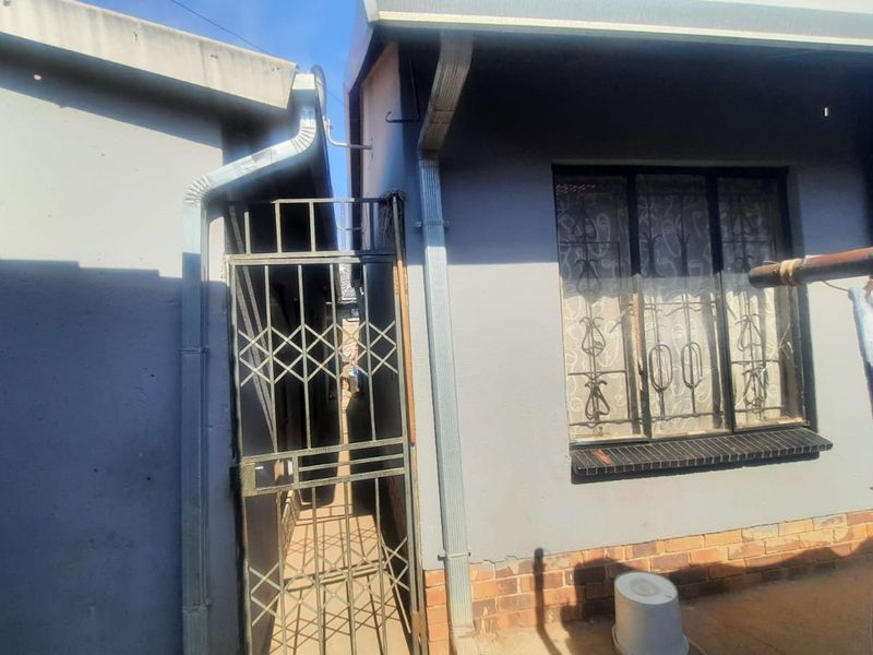 Rear exterior view of the property featuring a security gate, metal security bars on the window, and brick plinth detailing.