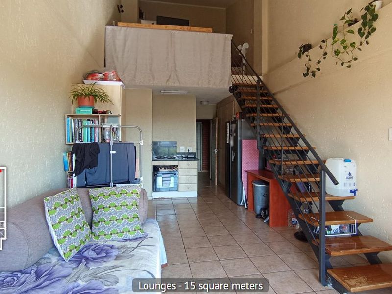 Open-plan living area featuring a mezzanine level, metal staircase, and compact kitchen with built-in cabinetry and appliances, finished with tiled flooring.