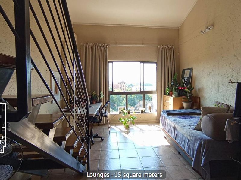 A living room area featuring tiled flooring, a large window with natural light, and an internal staircase leading to an upper level.