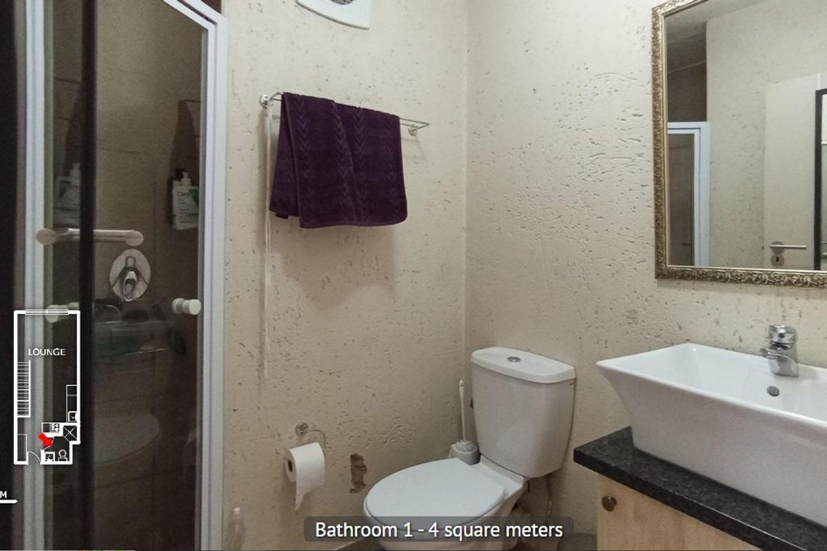 A compact bathroom featuring a shower enclosure, a vessel sink on a vanity cabinet, and a toilet, with visible wall damage requiring repair.
