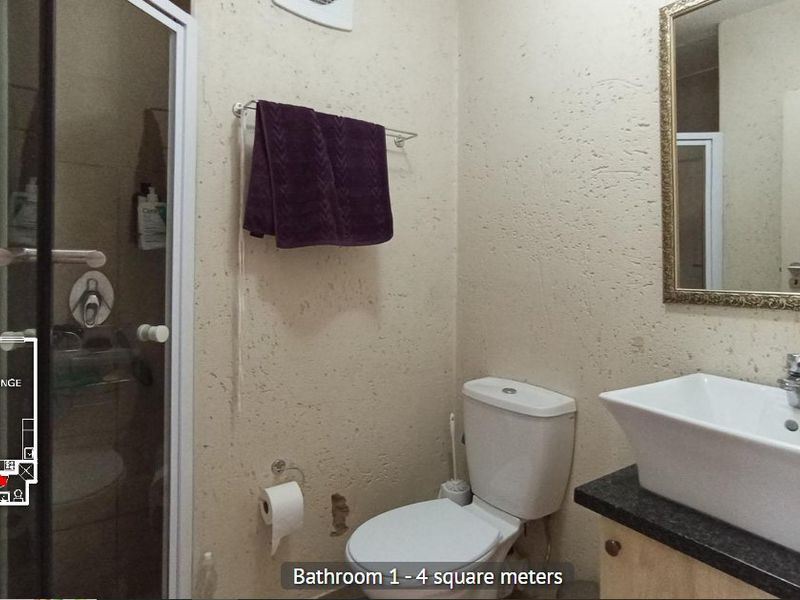 A compact bathroom featuring a shower enclosure, a vessel sink on a vanity cabinet, and a toilet, with visible wall damage requiring repair.