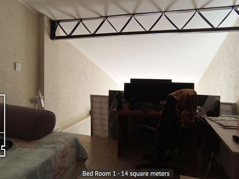 A bedroom featuring tiled flooring, textured walls, and an exposed steel roof truss, providing a unique architectural character to the space.