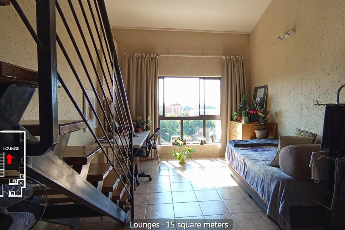 A living area featuring tiled flooring, a prominent staircase, and a large window providing natural light and an exterior view.