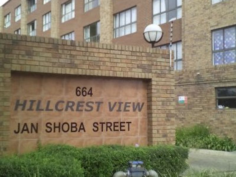 Exterior view of the Hillcrest View apartment complex entrance, featuring brick facade architecture and landscaped garden area.