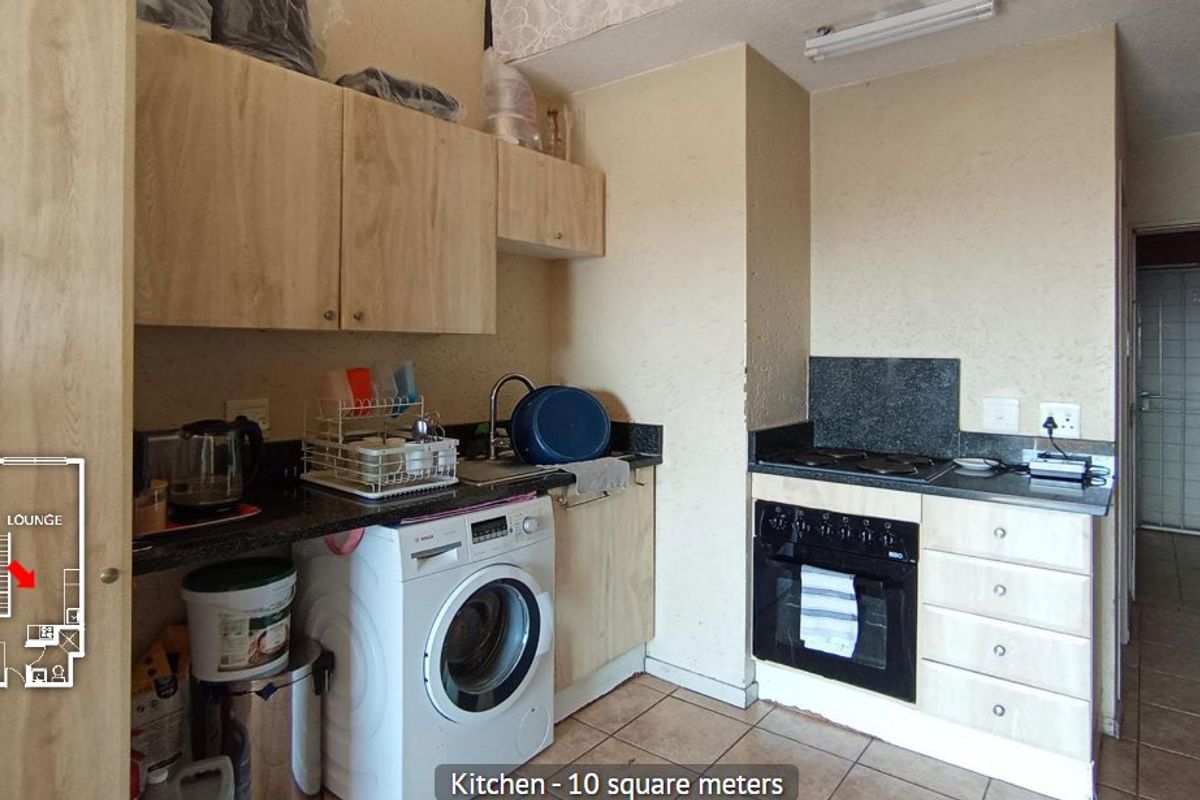 Compact kitchen featuring built-in cabinetry, granite countertops, integrated oven and hob, and tiled flooring, with an adjacent security gate entrance.