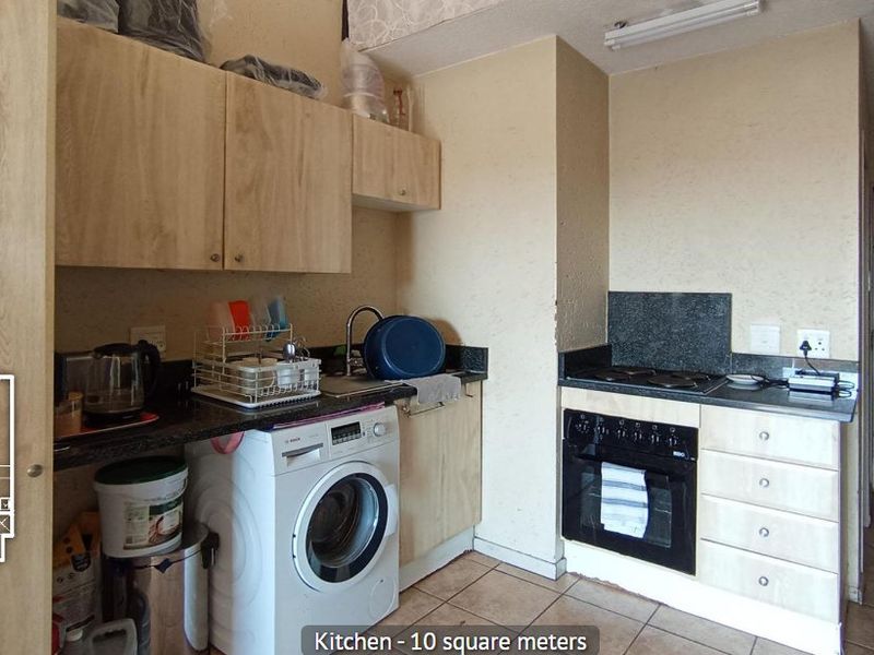 Compact kitchen featuring built-in cabinetry, granite countertops, integrated oven and hob, and tiled flooring, with an adjacent security gate entrance.