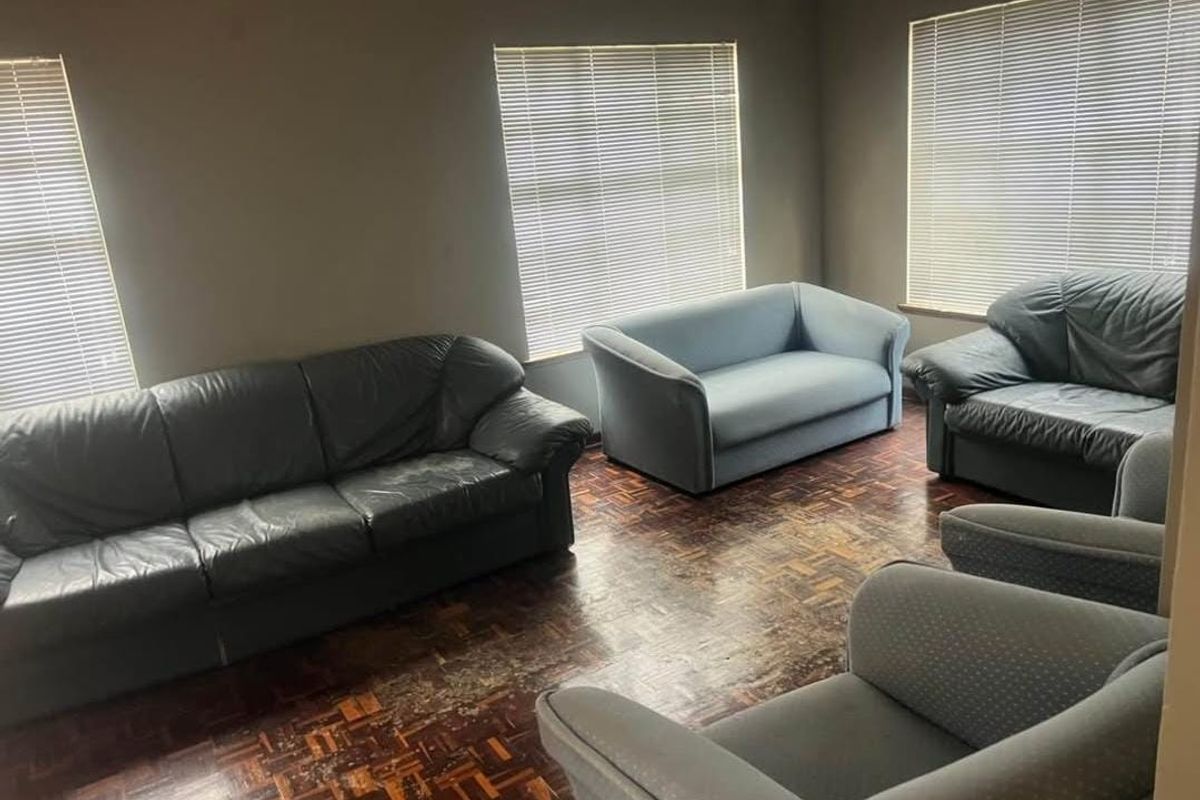 A living room featuring dark parquet flooring and multiple windows fitted with venetian blinds, offering a blank canvas for renovation.