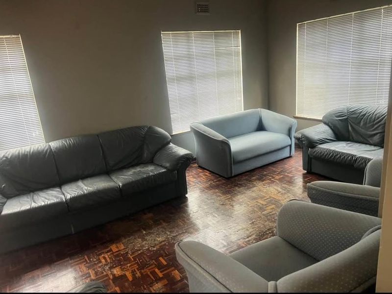 A living room featuring dark parquet flooring and multiple windows fitted with venetian blinds, offering a blank canvas for renovation.