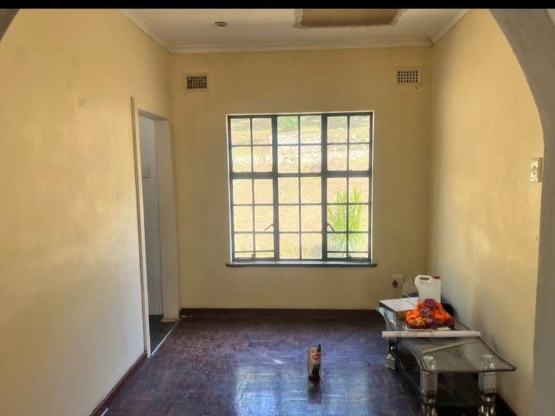 An empty living room featuring original parquet flooring, a large steel-framed window, and coved cornicing, requiring cosmetic updates to restore its appeal.
