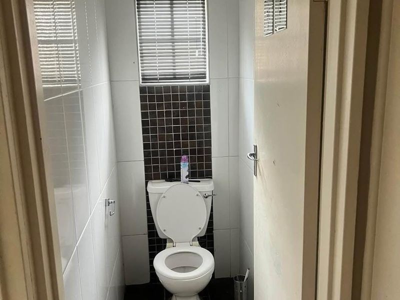 A compact, functional guest toilet featuring tiled walls and flooring, a window for natural light, and a built-in ventilation fan.