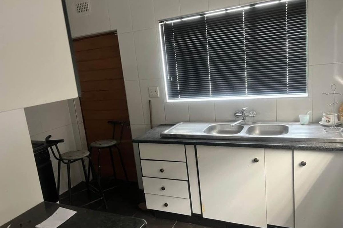 A functional kitchen featuring a stainless steel double sink, laminate countertops, tiled splashback, and built-in cabinetry with a window for natural light.