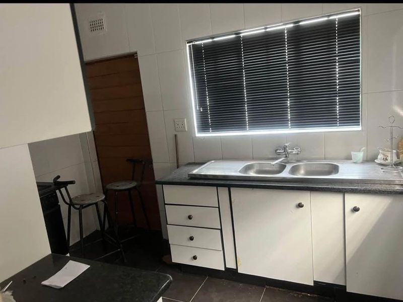 A functional kitchen featuring a stainless steel double sink, laminate countertops, tiled splashback, and built-in cabinetry with a window for natural light.