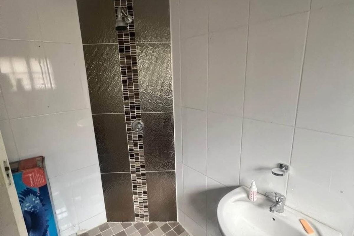 A compact bathroom featuring a pedestal basin and a tiled shower enclosure with decorative mosaic accents.