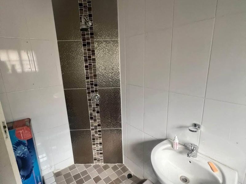 A compact bathroom featuring a pedestal basin and a tiled shower enclosure with decorative mosaic accents.